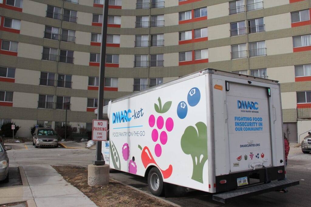 DMARC mobile food pantry vehicle parked outside large apartment building.