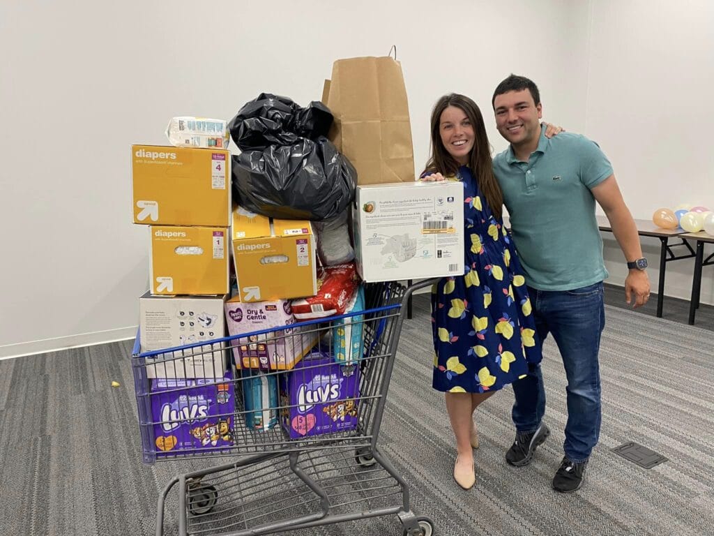 couple stands next to donated diaper boxes in a full shopping cart